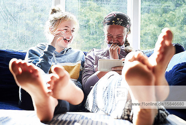 Teenager-Mädchen  die auf einer Couch lachen und etwas auf einem Telefon anschauen