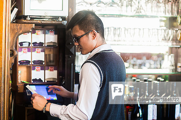 junger asiatischer Kellner in einer Bar mit einer Rechnung