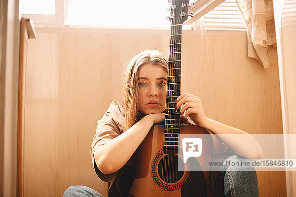 Junge Frau lehnt auf Gitarre  während sie auf dem Boden auf dem Balkon sitzt