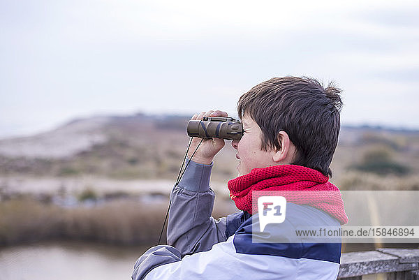 Playful boy looking through binoculars to the sea