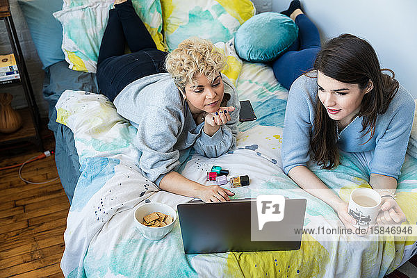 Hochwinkelansicht von Freunden mit Laptop  während sie zu Hause auf dem Bett liegen