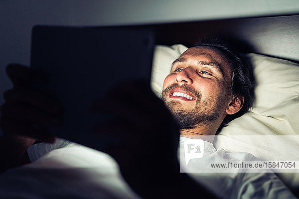 Junger  gut aussehender und müder Mann mit Bart  der nachts auf einer Tafel lächelt