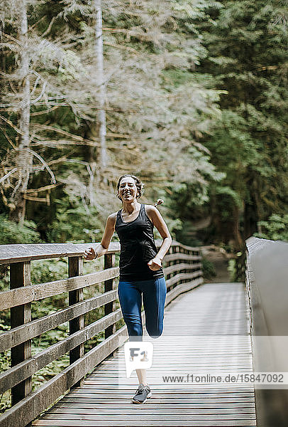 Eine fitte Läuferin überquert eine Fußgängerbrücke im Wald