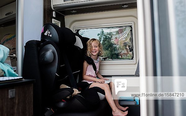 young girl sitting in a car seat in a camper van smiling holding ipad