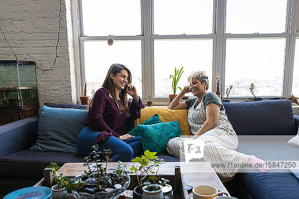 Lächelnde Freundinnen sitzen zu Hause zusammen auf dem Sofa vor dem Fenster