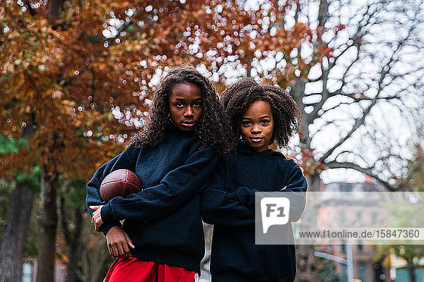 Portrait of confident sisters with American football in park