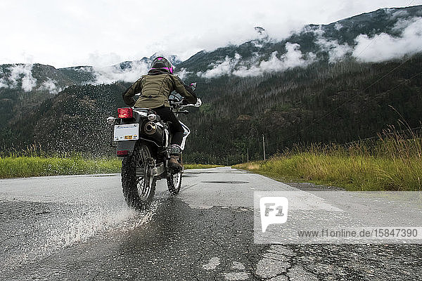 A woman rides her motorcycle on a cloudy summer day.