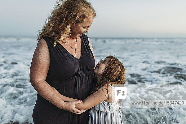 Seitenansicht einer glücklichen jungen Tochter  die ihre Mutter in der Abenddämmerung im Meer umarmt