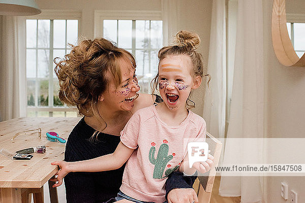 Mutter und Tochter lachen  während sie zu Hause mit Make-up spielen