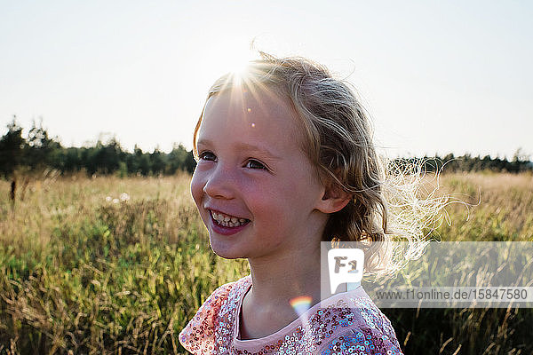 Porträt eines jungen  lockig behaarten blonden Mädchens  das bei Sonnenuntergang draußen lächelt