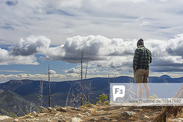 Männlicher Wanderer steht auf Berggipfel mit dramatischen Wolken