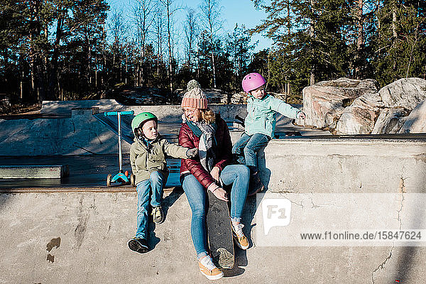 Mama und ihre Kinder spielen und haben Spaß in einem Skatepark im Freien