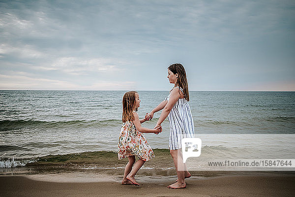 Seitenansicht der Schwestern  die am Strand des Lake Michigan tanzen