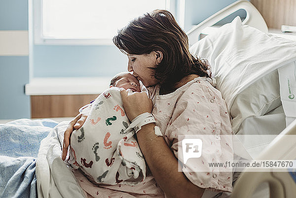 Side view of mother in hospital bed kissing newborn son's head