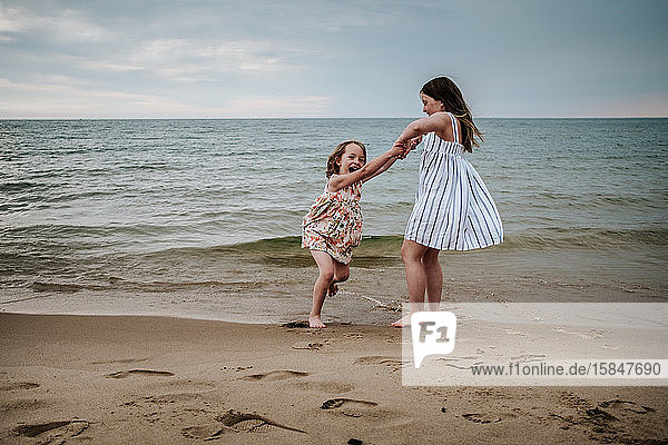 ältere Schwester schwingt jüngere Schwester am Strand am Lake Michigan