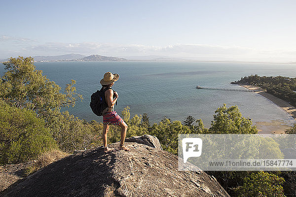 Backpacker with hat and swimsuit  on top of rocky hill during sunset