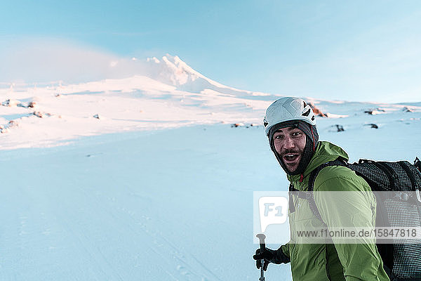 Skifahrer schaut lächelnd in die Kamera  während er sich den Berg hinauf häutet