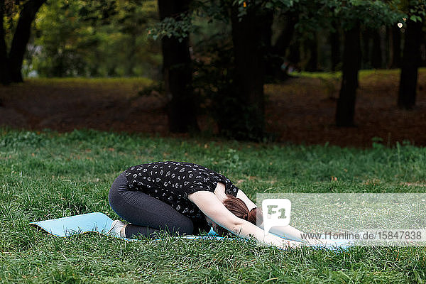 Das entspannte Mädchen macht Yoga im Park auf einem Teppich
