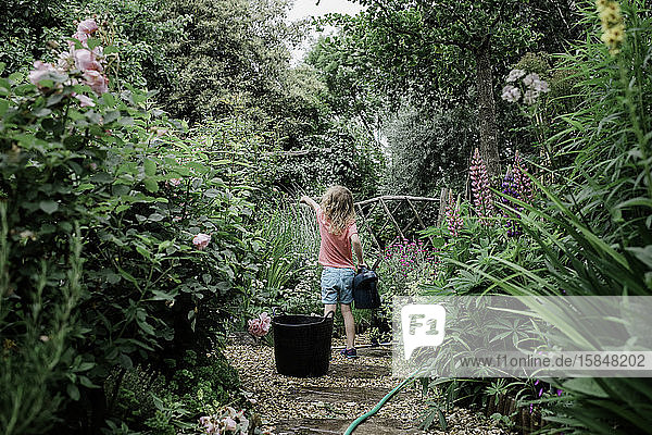 Ein junges Mädchen bewässert im Sommer ihren englischen Bauerngarten