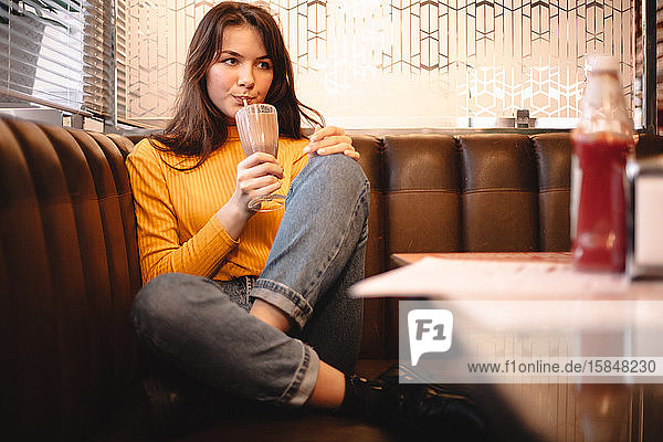 Nachdenkliches Teenager-Mädchen trinkt Schokoladenmilchshake im Restaurant