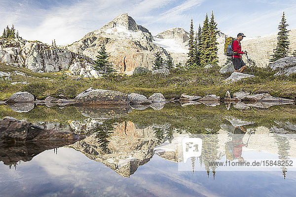 Side view and reflection of backpacker hiking beside alpine lake.