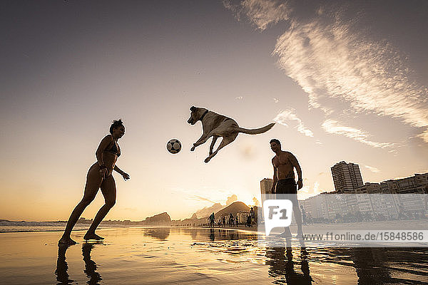 Fußballspiel eines Paares mit Hund an der Uferpromenade am Strand von Copacabana