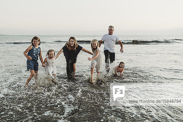 Family with four girls playing and splashing in waves at sunset