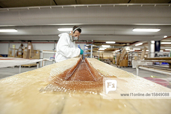 Ein Mann trägt Fiberglas auf eine Form in einer Bootsbaufabrik auf
