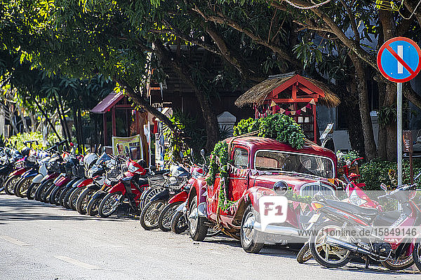 Motorräder und Oldtimer  die entlang einer Straße in Luang Prabang geparkt sind