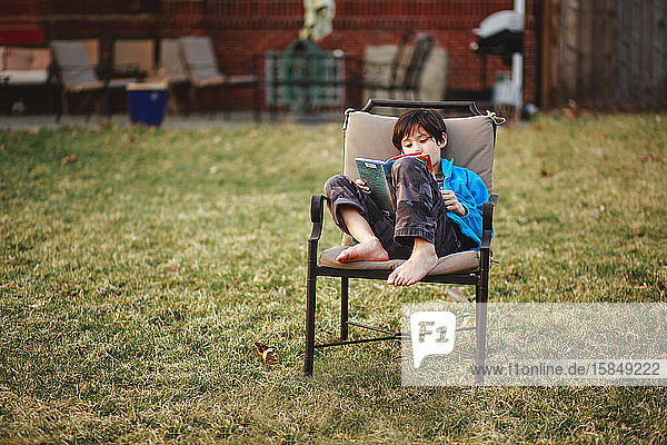 Ein glücklicher Junge liest bei kühlem Wetter barfuss im Hinterhof ein Buch