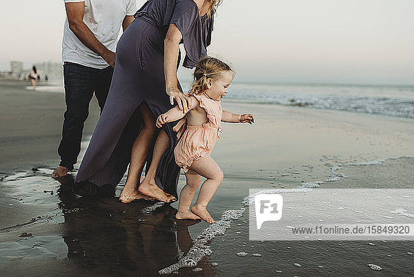 Seitenansicht eines Kleinkindes mit Familie  das bei Sonnenuntergang in den Ozean läuft