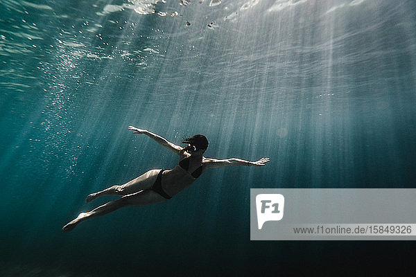 Frau in voller Länge unter Wasser im Ozean schwimmend