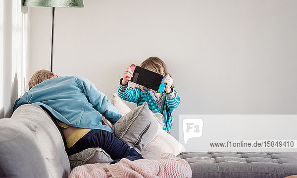 brother and sister playing Nintendo switch at home on the sofa
