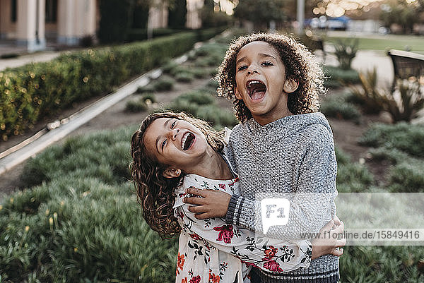 Süße Geschwister lächeln und lachen  während sie sich draußen im Sonnenschein umarmen