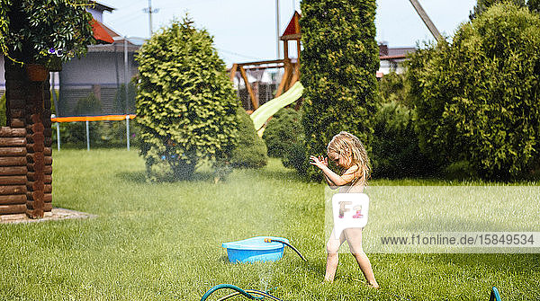 Kleines Mädchen spielt mit Wasser im Hof des Hauses