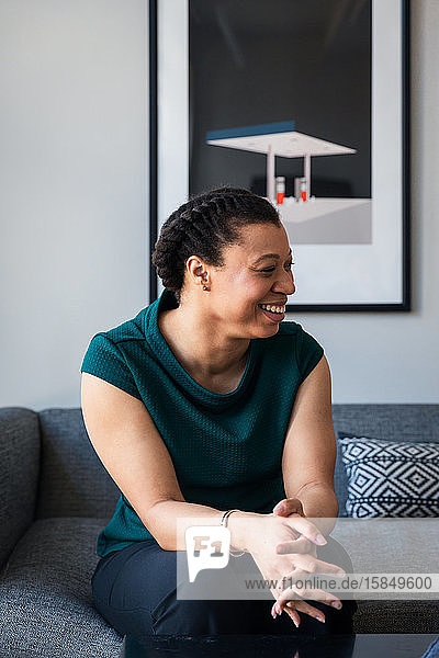 Lächelnde selbstbewusste Unternehmerin sitzt im Büro auf dem Sofa an der Wand