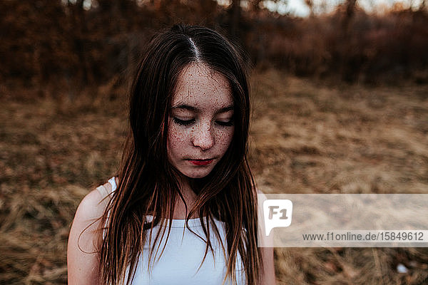 Portrait of freckled young girl look down in a field
