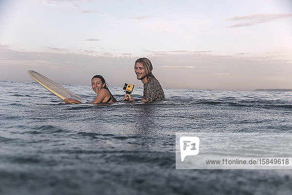 Glückliches Paar mit Surfbrett und Kamera im Meer