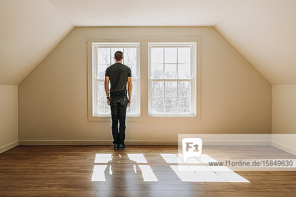 Mann steht vor einem Innenfenster in einem leeren  einsamen  minimalistischen Raum