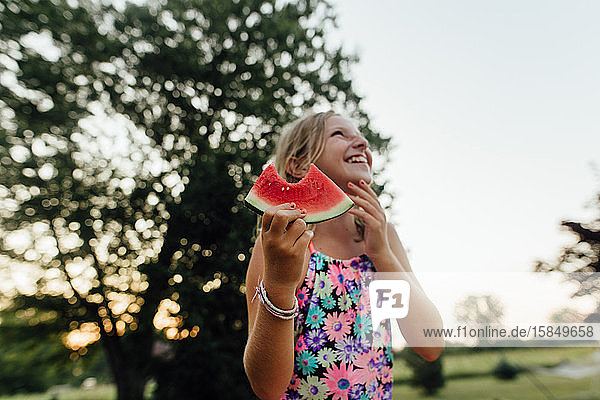 Junges Mädchen mit großem Lächeln isst im Sommer draußen Wassermelone