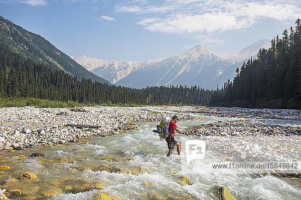 Backpacker crosses icy river in British Columbia  Canada.