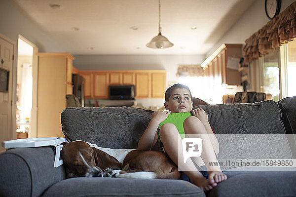 Junge entspannt sich neben seinem Hund  während er zu Hause sein Tablett auf der Couch hält