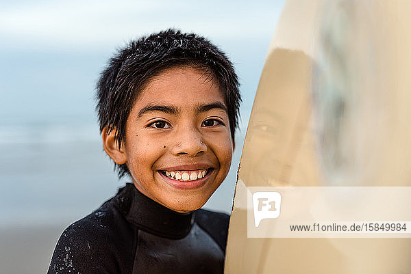 Porträt eines glücklichen Jungen  der ein Surfbrett hält