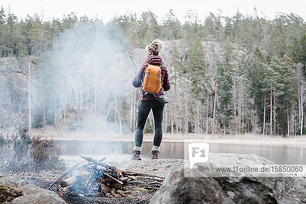 Frau  die auf einem Felsen am Lagerfeuer steht  während sie in Schweden wandert