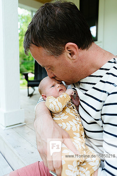 A new dad kissing his newborn baby girl on the forehead