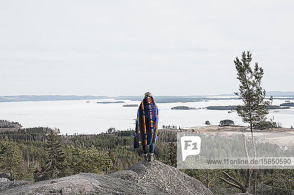 woman wrapped in a blanket looking at the view of the ocean and forest