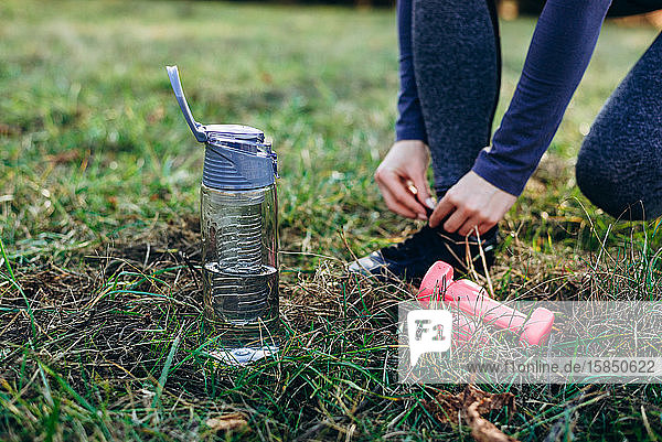 Fitness im Park  Mädchen beim Schuhbinden  Fußflasche und Hanteln  Nahaufnahme.