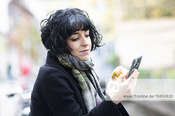 junge Frau mit Apfel und Smartphone draußen