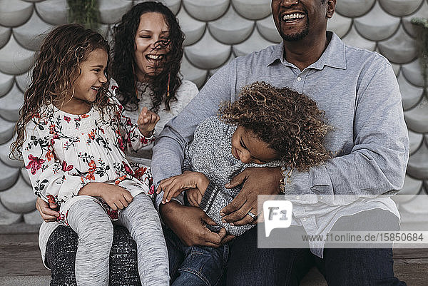 Lifestyle image of happy family tickling each other and laughing while