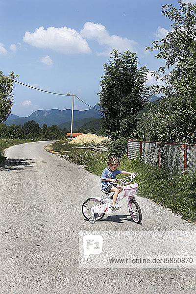 Ein kleiner Junge fährt Fahrrad auf einer leeren Straße in den Bergen